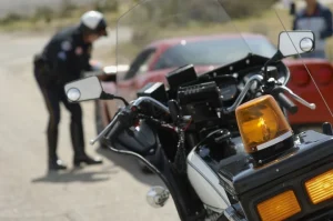 A motorcycle police officer writing a ticket beside a stopped red car