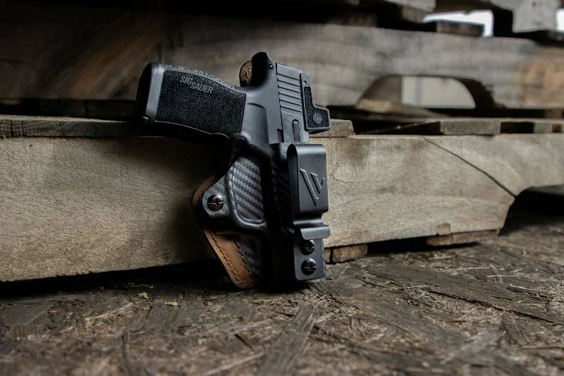 A handgun in a black holster resting on a weathered wooden plank