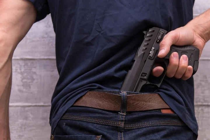 A man drawing a handgun from the back of his waistband